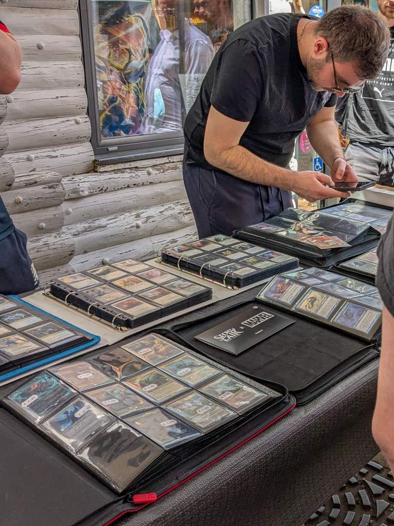 Frantz, patron de la boutique, devant une table de classeurs de cartes Magic et, un peu plus loin, Pokémon.